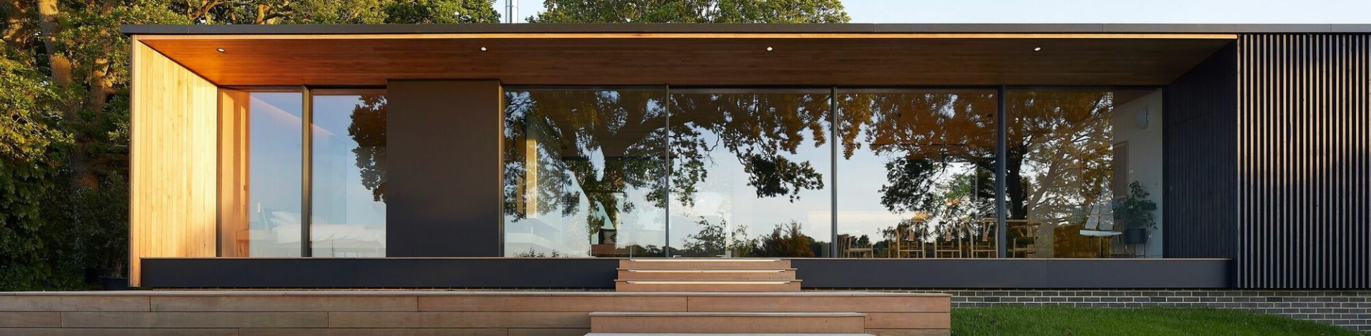 Ein modernes Haus mit großen Glasfenstern, Holzfassade und einer überdachten Terrasse